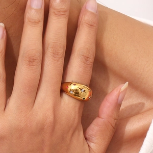 Detail shot of a chunky gold ring with star patterns and colorful gemstones on a finger