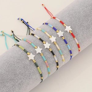 Handmade beaded bracelet set with white shell stars and gold accents on a grey display