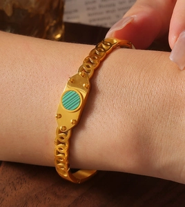 Close-up of golden bangle with green striped inlay and chain-style band on wrist