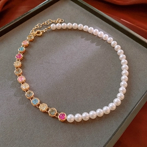 Macro detail of gold necklace with split design featuring white pearls and colorful gems