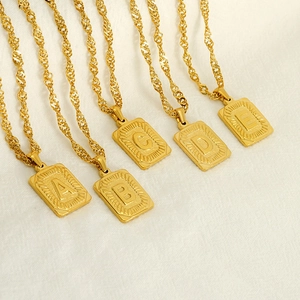 Multiple gold stainless steel letter pendants with water wave chains on beige fabric