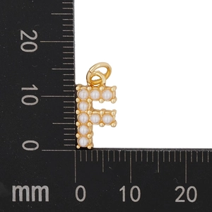 Macro shot of gold letter F pendant with pearls next to a metric scale for size