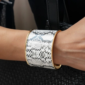 Macro detail of wide golden bangle featuring grey snakeskin pattern on model's wrist
