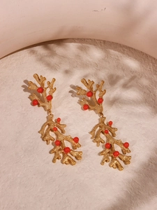 Macro detail of gold-plated coral branch earrings with red beads and oil dripping finish