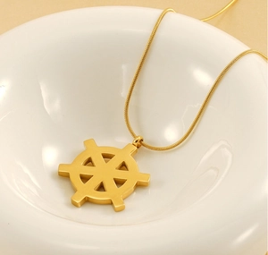 Detail of 18K gold-plated rudder pendant and sleek snake chain on white ceramic base