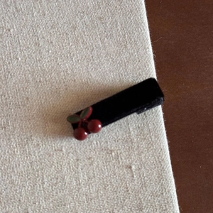 Detailed close-up of a black velvet hair claw clip with a decorative red cherry charm