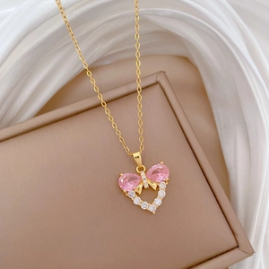 Close-up of heart and bow pendant with pink zircon on a gold-plated necklace chain