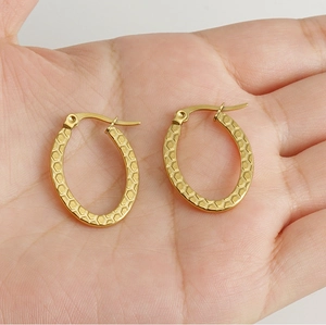Close-up of golden hoop earrings with embossed hexagon honeycomb texture on palm