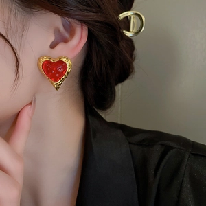 Detail of red heart earring with hammered gold frame worn by a model in close-up view