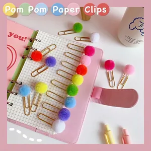 Colorful pom pom metal paper clips on a pink notebook for office and school stationery