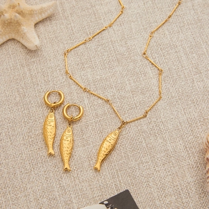 Detailansicht eines 18K Gold Fisch-Anhänger-Halsketten und Ohrring-Sets am Strand
