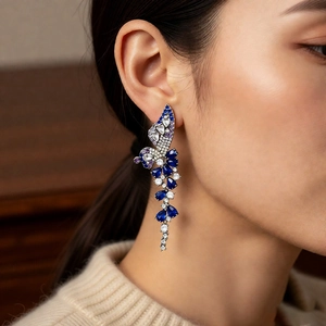 Detail of long tassel wing earrings with blue zircons worn by a model on a brown background
