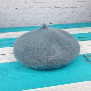 Detailed top view of light grey faux fur beret with fluffy texture and decorative pom-pom