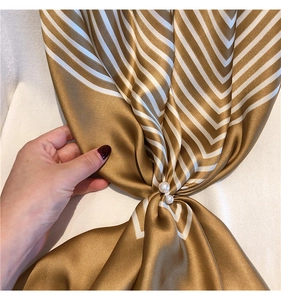 Detail of silk-textured striped scarf in brown and white with pearl pins decor