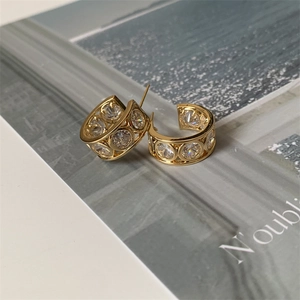 Detail of gold C-shaped earrings with clear zircon stones on vintage paper background