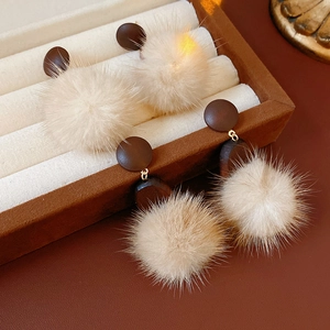 Detail of round beige pompom drop earrings with soft fur texture on brown leather surface