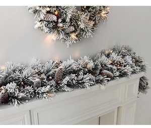 Detail of snowy Christmas garland with pine cones and warm LED lights on a white fireplace