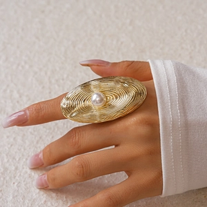 Macro shot of gold oval ring with concentric textures and a white faux pearl center