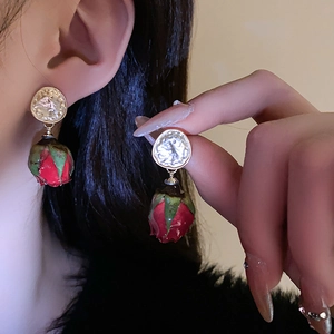 Détail de la boucle d'oreille bouton de rose rouge avec clou en métal doré irrégulier