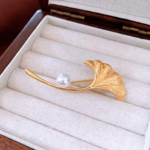 Detailansicht der 18K vergoldeten Ginkgo-Brosche mit glänzender Perle auf Samt