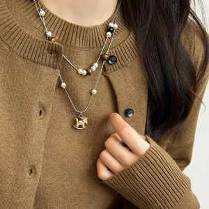 Detail of double-layer necklace with wooden horse pendant and tiger eye beads on a brown sweater