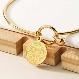 Macro shot of gold Saint Benedict medal charm on a polished stainless steel bangle