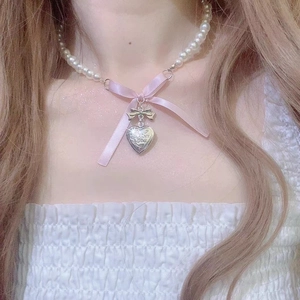 Detail of a pink silk bow pearl necklace with a silver heart pendant on a model's neck