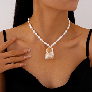 Detail of a pearl necklace with a shell pendant worn by a model in black attire