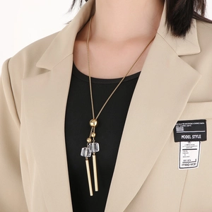 Long gold necklace featuring transparent square pendants and cylinders on a beige blazer