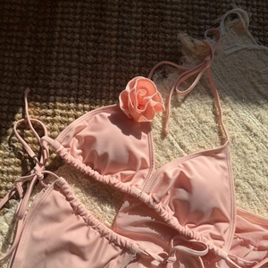 Flat lay of pink 3-piece bikini set with 3D floral accent on woven summer mat
