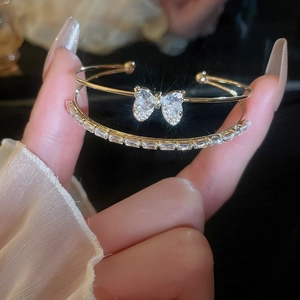 Detail of gold double-layered cuff bracelet featuring butterfly charms and crystal chains