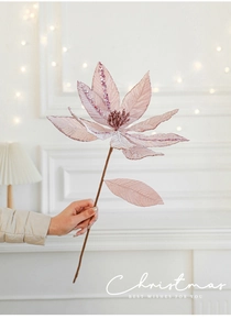 Detail of light pink velvet Christmas flower with glitter edges held against a bokeh background
