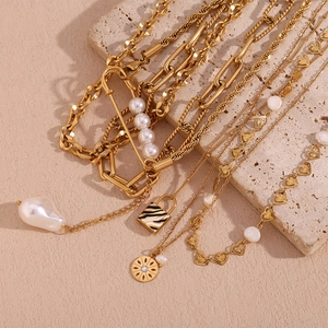Detail of tiered gold-plated steel necklaces featuring pearls and enamel lock charm