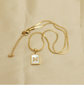 Detail view of a gold square shell pendant with letter M on a sleek snake chain necklace