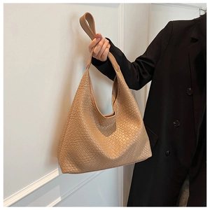Detail of the woven texture on a beige leather hobo bag held by a model in a black suit