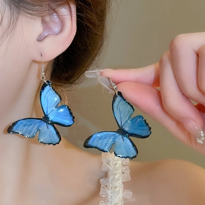 Macro shot of delicate gradient blue butterfly earrings worn on a model's ear
