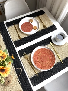 Detailed view of woven paper rope placemat with black stripes and orange coaster set