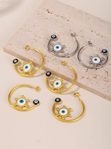 Macro detail of 18K gold and silver C-shaped earrings with blue enamel evil eye design