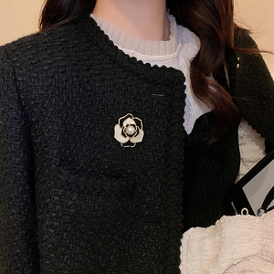 Détail d'une broche camélia en émail blanc avec perle sur une veste en tweed