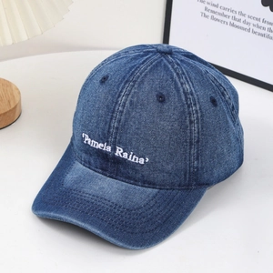 Vintage washed blue denim baseball cap featuring white Pamela Raina embroidery in a casual setting