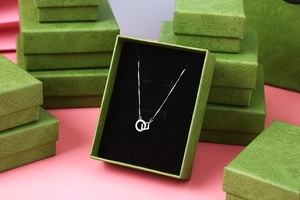 Silver geometric pendant necklace displayed in vintage green embossed jewelry packaging