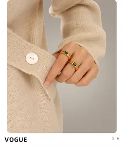 Detail of two stacked 18K gold plated rings with emerald green stones on a model