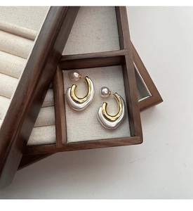 Detail of C-shaped resin earrings with golden metal and pearls in a wooden box