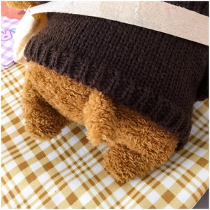 Close-up of a plush Shiba Inu dog bag showing a brown knit sweater and small tail detail