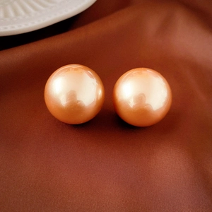 Macro shot of champagne pearl stud earrings on a dark brown silk fabric background