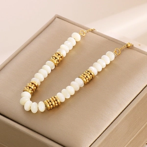 Elegant gold-plated titanium steel necklace with white beads on a beige jewelry box