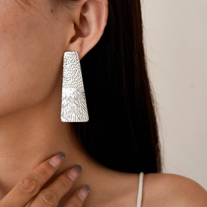 Macro detail of geometric silver earrings featuring a textured hammered metal surface