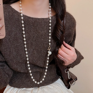 Détail d'un long collier de perles avec fermoir à bascule doré sur un pull marron