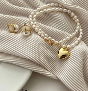 Detail of elegant gold heart pendant and double pearl necklace on white fabric