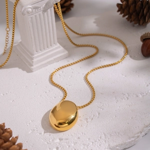 Détail d'un collier à pendentif ovale plaqué or 18 carats sur une surface texturée blanche